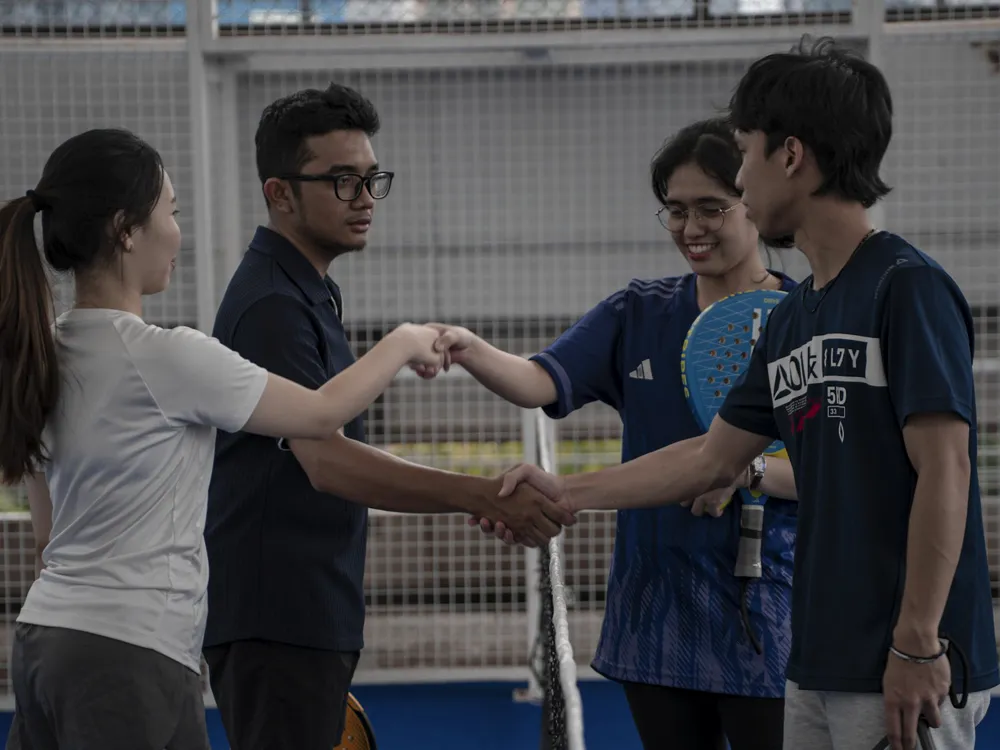 Four friends shake hands at the net after a padel match